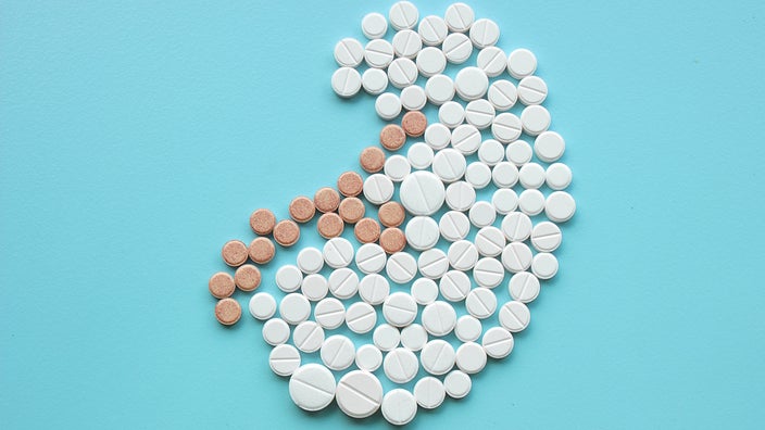 Pictured are white and brown pills placed in the shape of a kidney on a blue background.