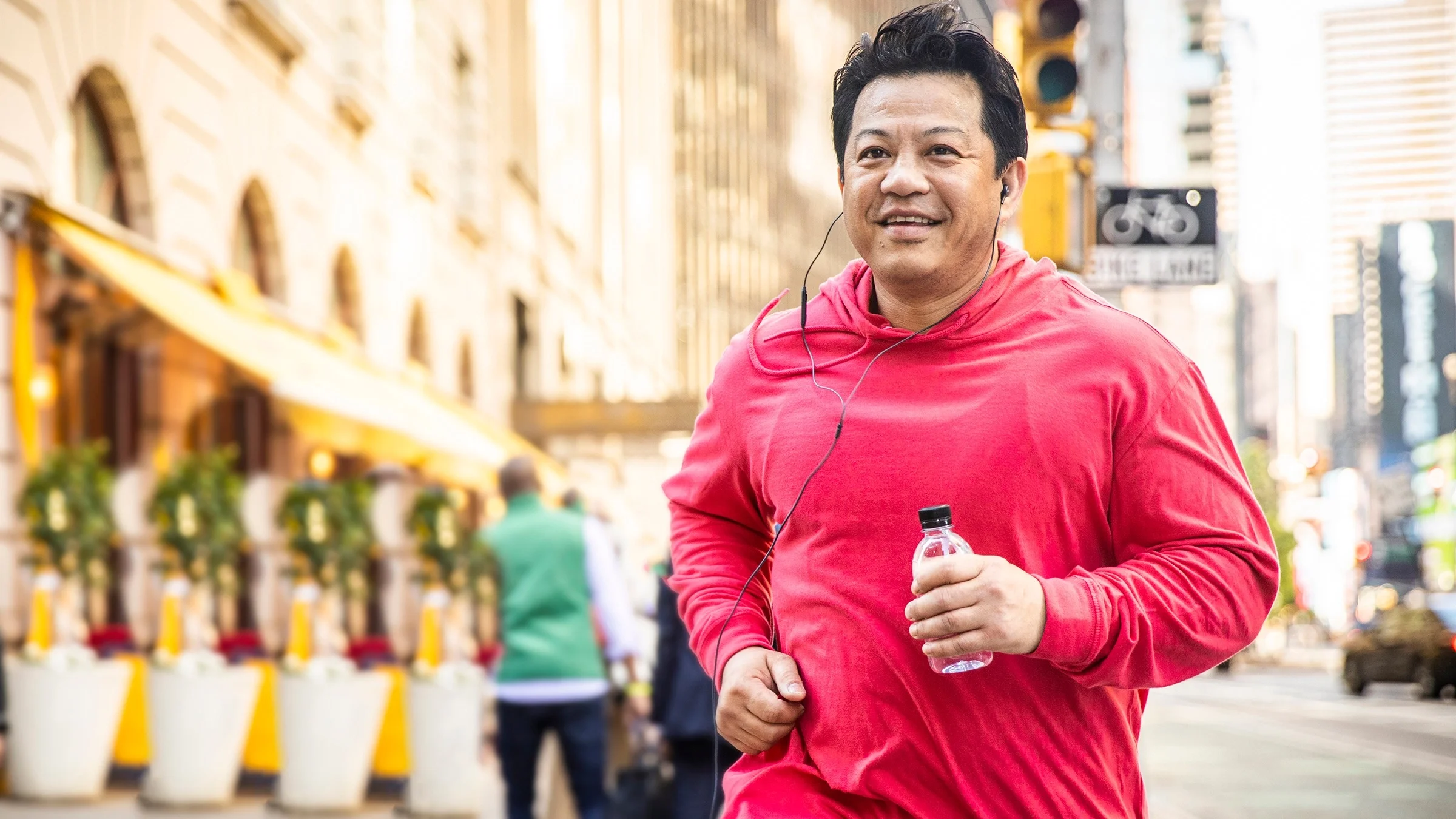 Middle aged man on a run through New York City. He is wearing a red hoodie.