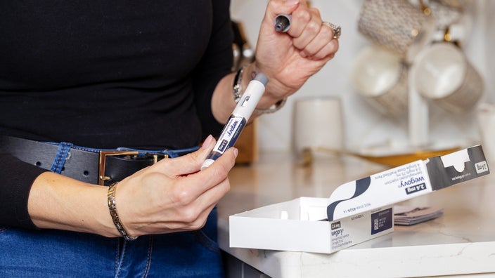 A woman, in close-up, inspects a Wegovy injection pen and medication box on a countertop.