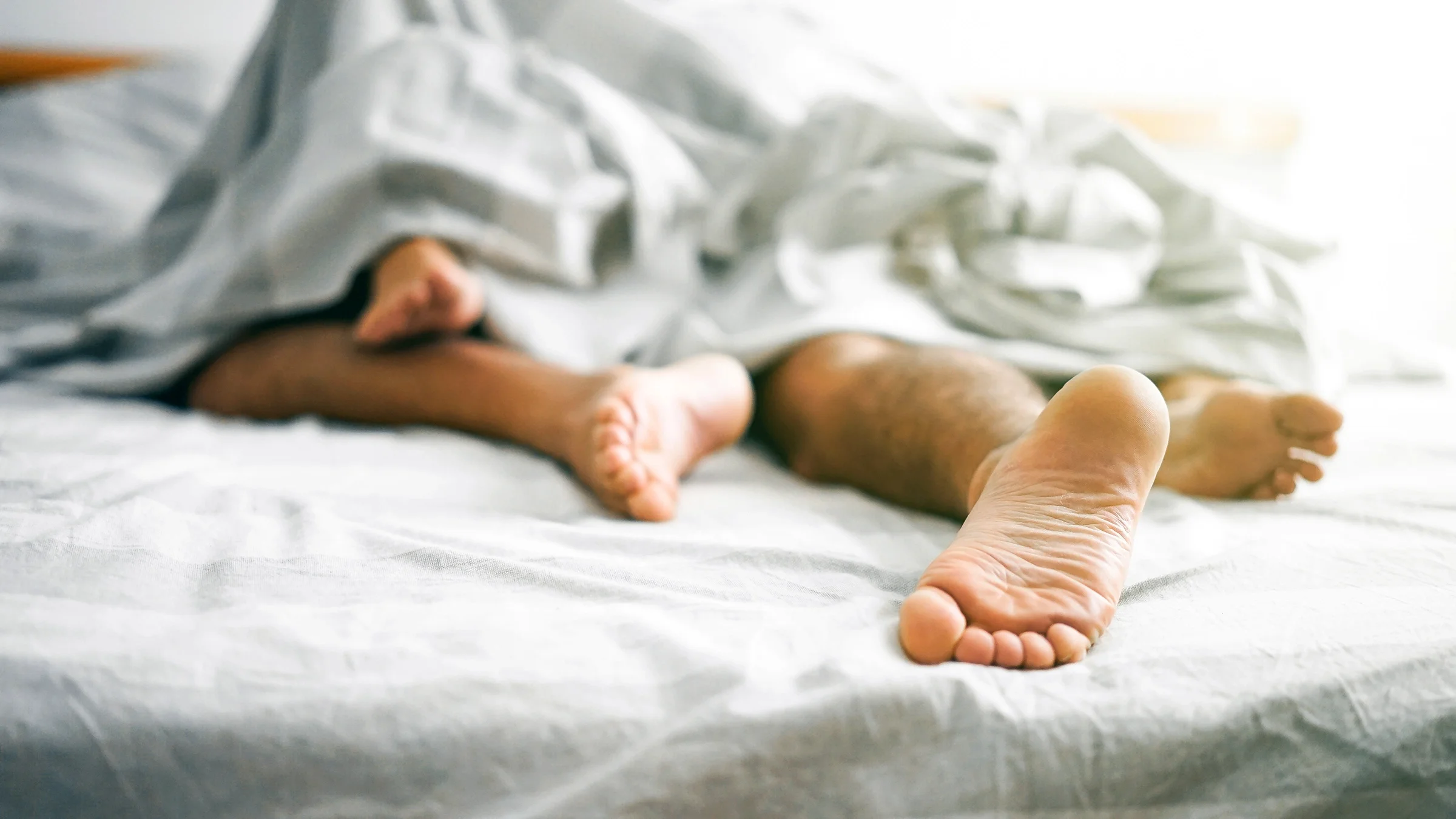 A close-up of a couple's feet under the covers at the end of the bed.