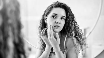 woman looking at pimples in mirror-1136758222