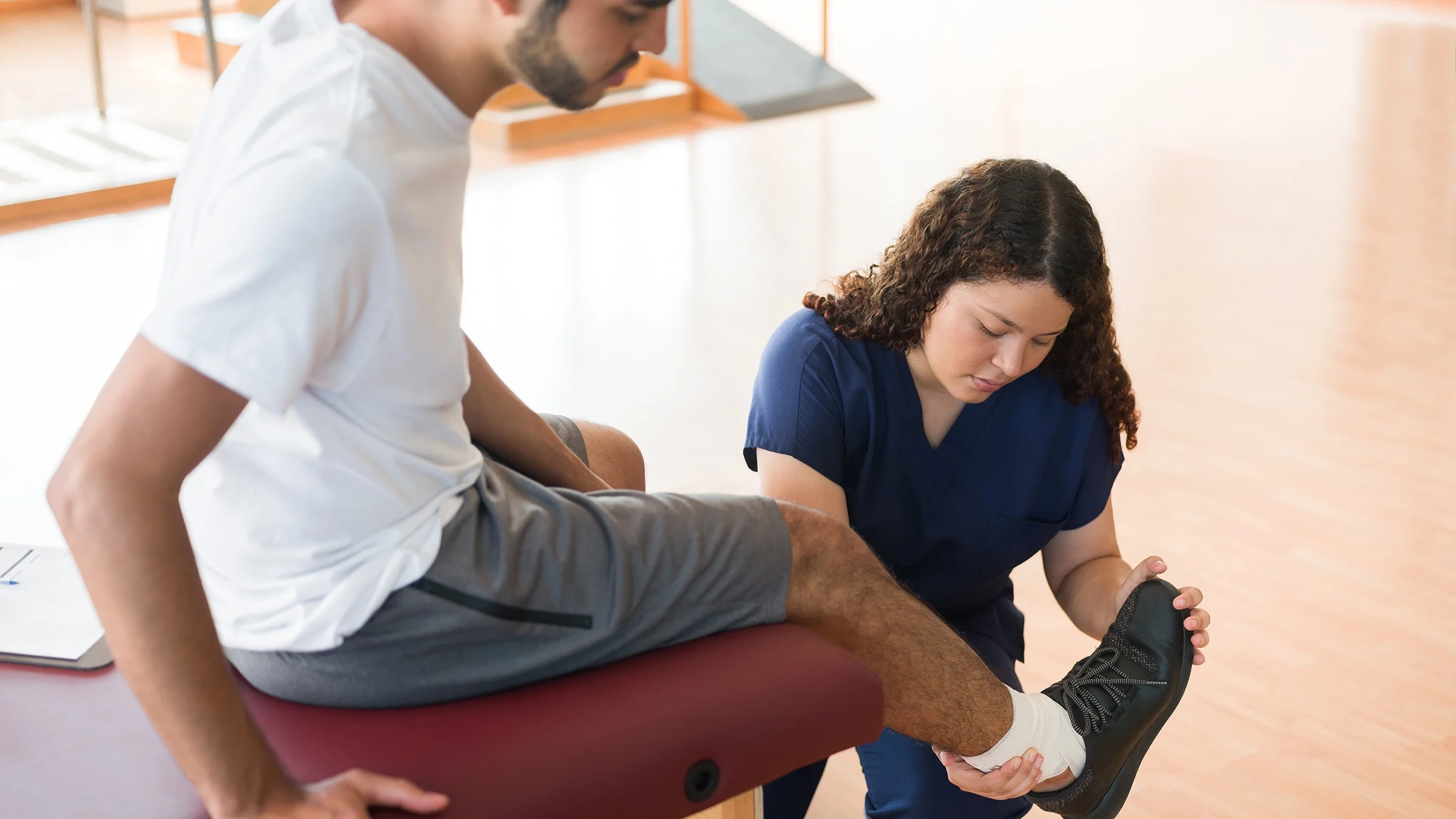 A physical therapist helps a man put on a sneaker.