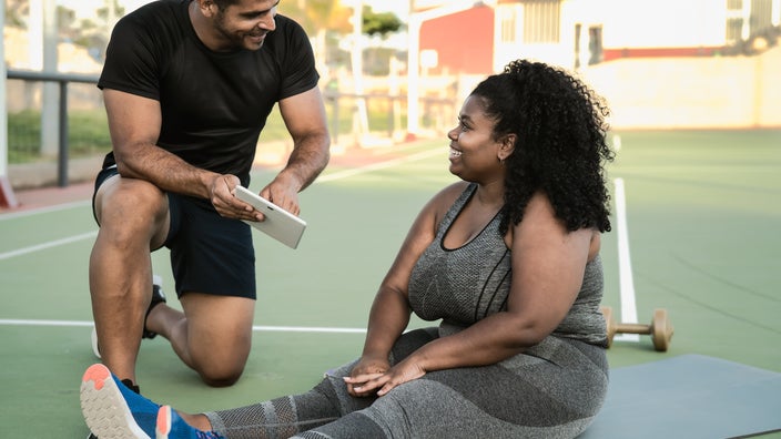 Personal trainer giving fitness instructions to a woman sitting down on a yoga mat.