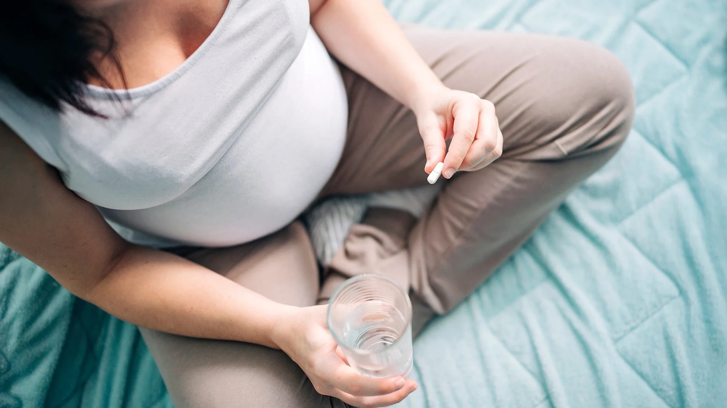 Top down view of a pregnant woman taking a white supplement pill.