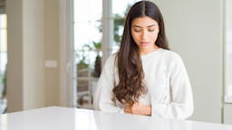 Woman with a stomach ache grabbing her stomach as she stands in the kitchen.
AaronAmat/iStock via Getty Images