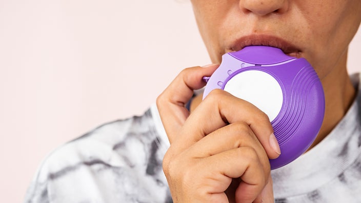Close-up of woman using purple inhaler.