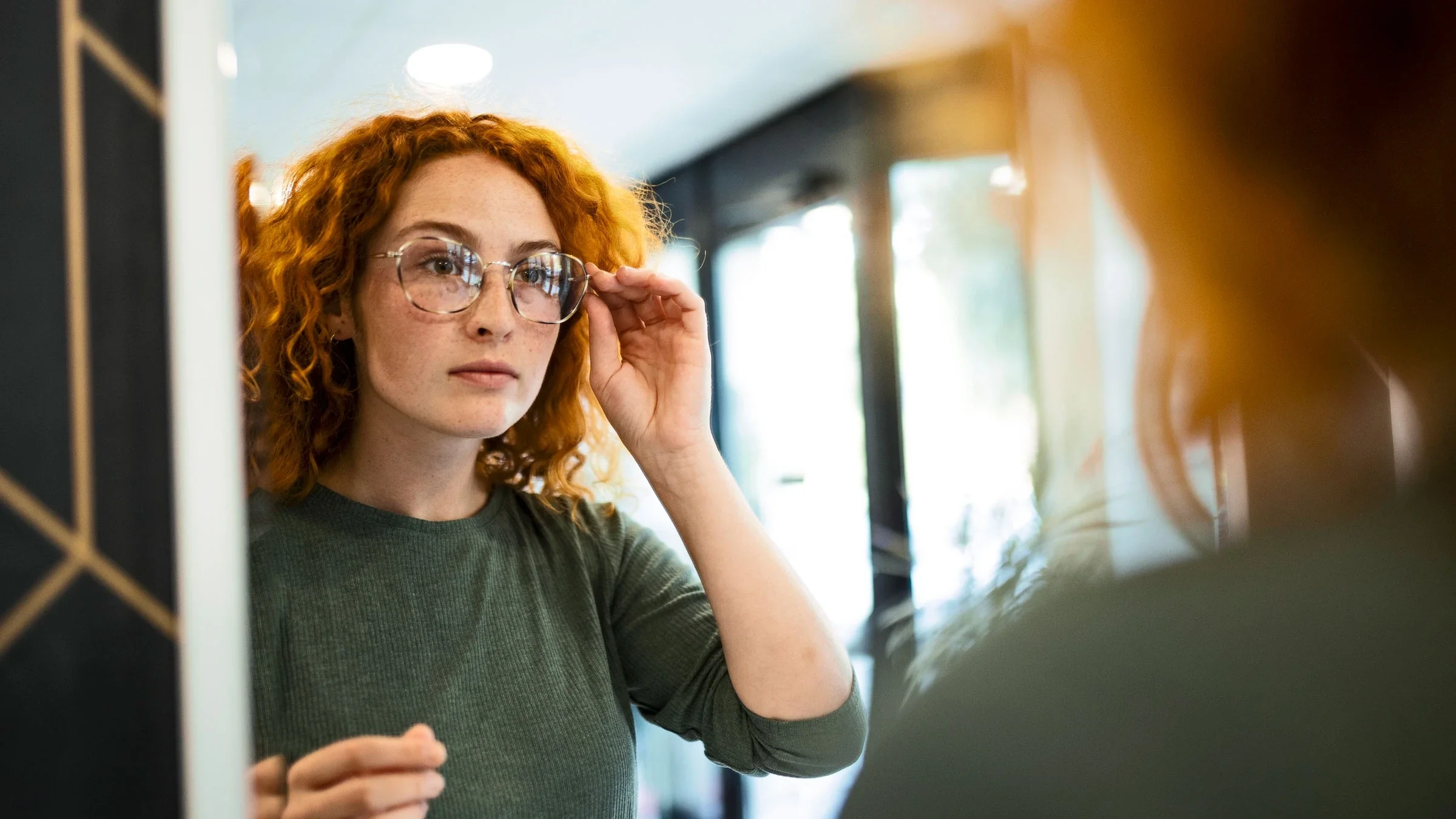 A woman tries on eyeglasses in a mirror.