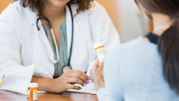 Doctor reviewing a prescription with the patient. The image is cropped in a way where we can't see either person's face. The focus is on the orange prescription bottle in the middle.
SDI Productions/E+ via Getty Images

