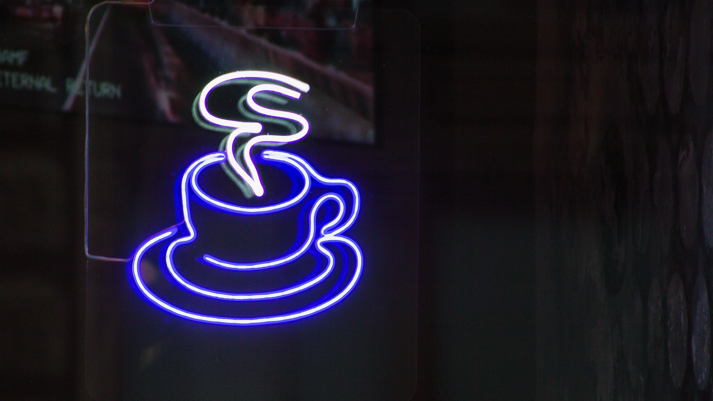 Neon coffee cup sign at night. The cup is a glowing blue with white steam.