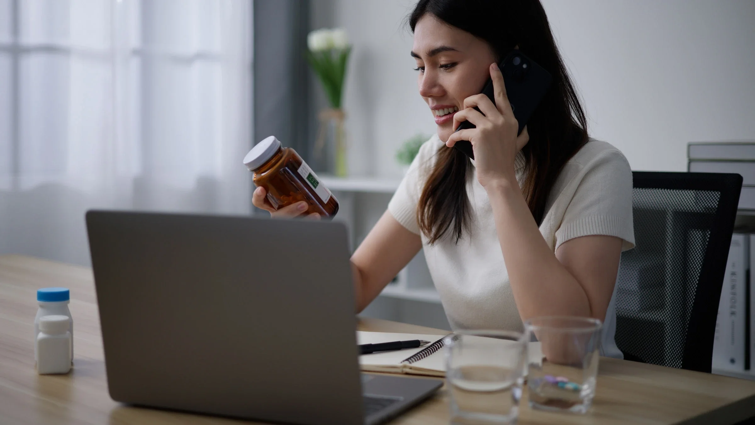 A person reading a supplement bottle while on a phone call.
