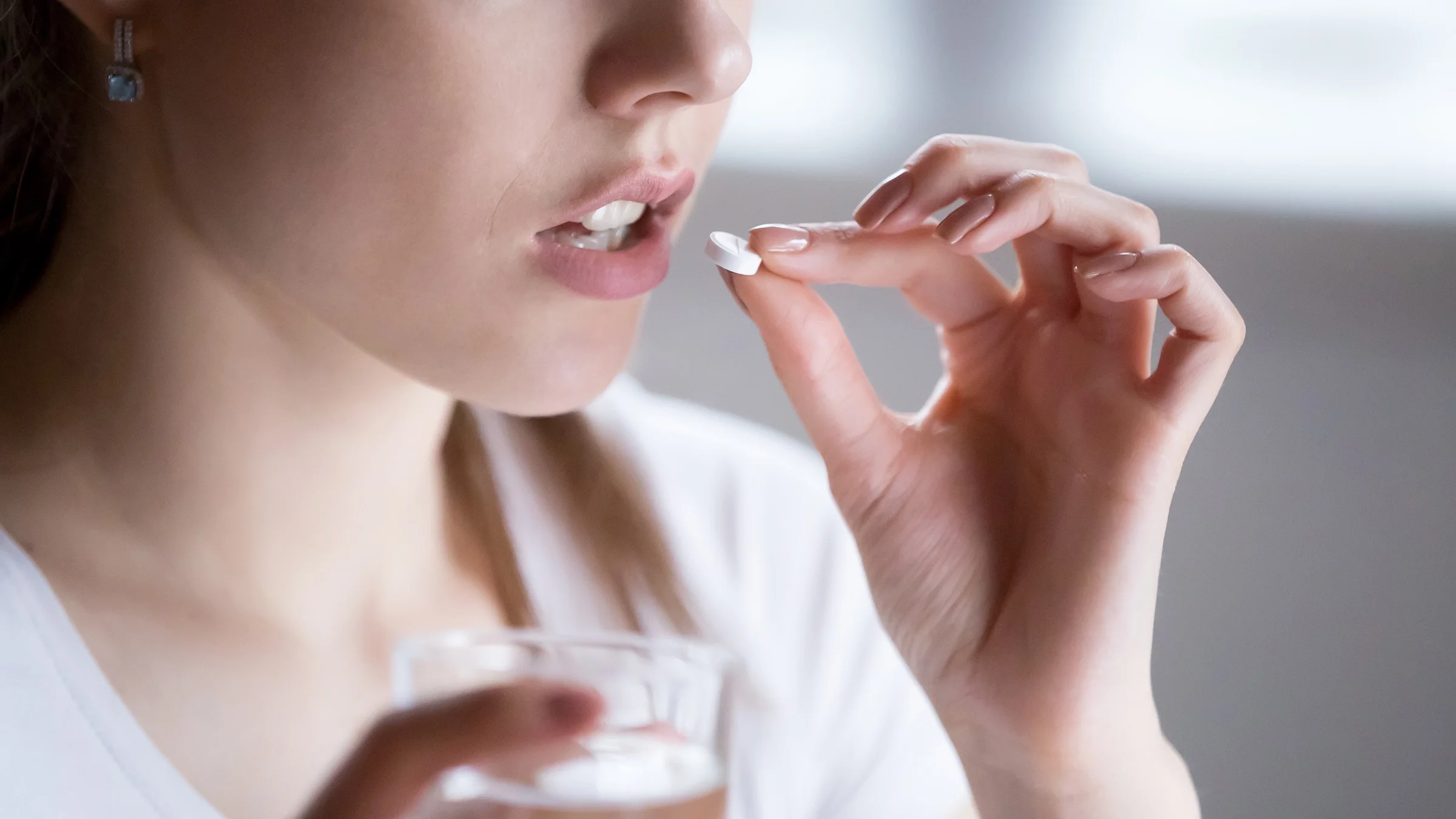 Cropped shot of a woman taking a white pill. She is wearing a white shirt.