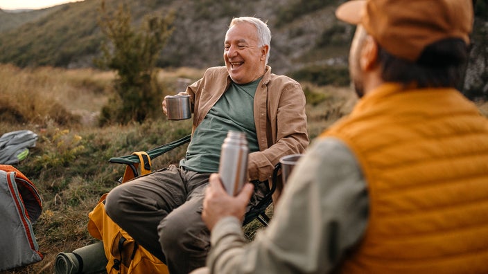 Older adult men camping and having fun drinking coffee around the campground.
