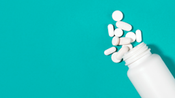 White medicine bottle with white pills spilling out on a teal background.
anilakkus/iStock via Getty Images