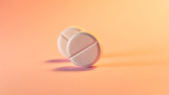 Two round white pills standing up on the edge on an orange pink background.