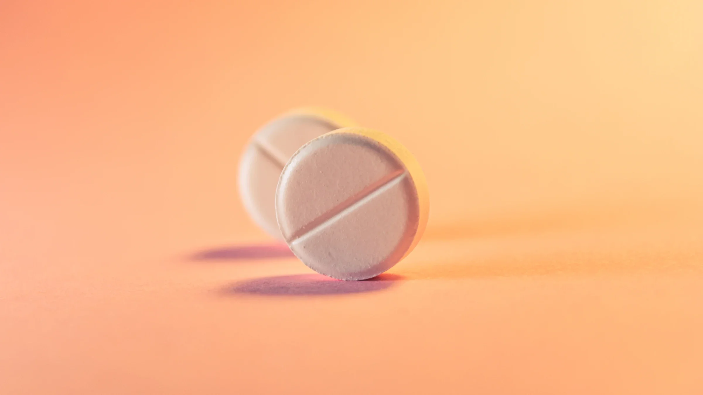 Two round white pills standing up on the edge on an orange pink background.
Oleg Rebrik/iStock via Getty Images