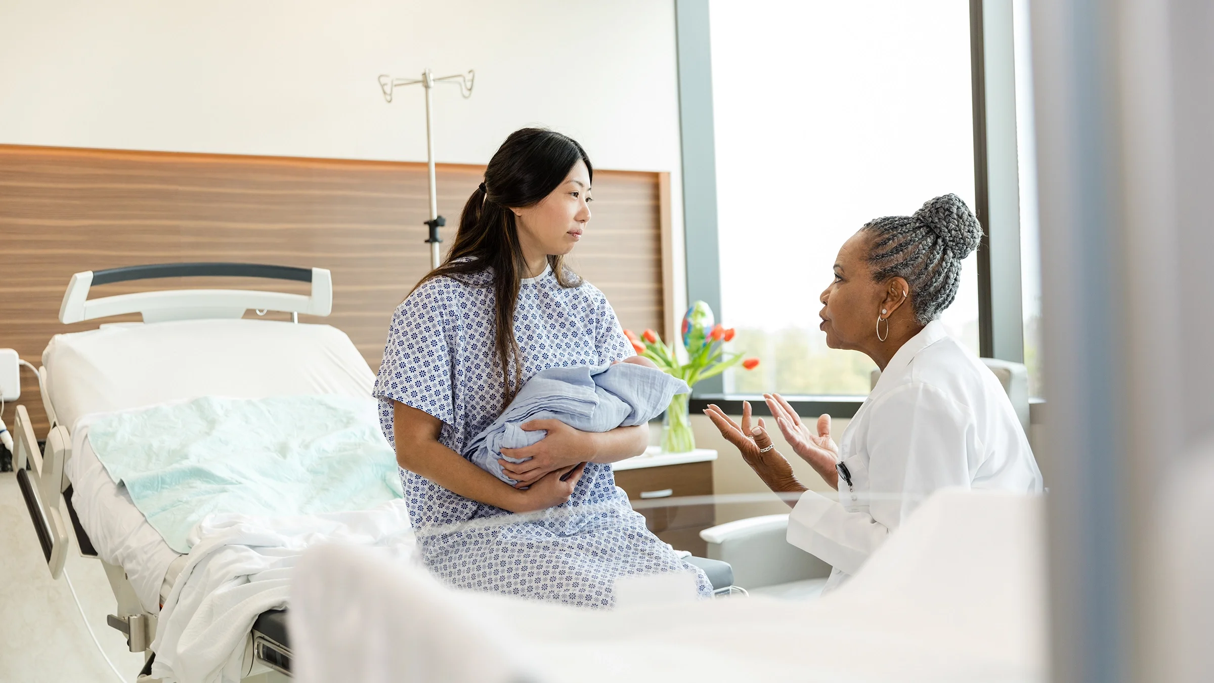 A healthcare professional talks to a woman holding a baby in a hospital room. 