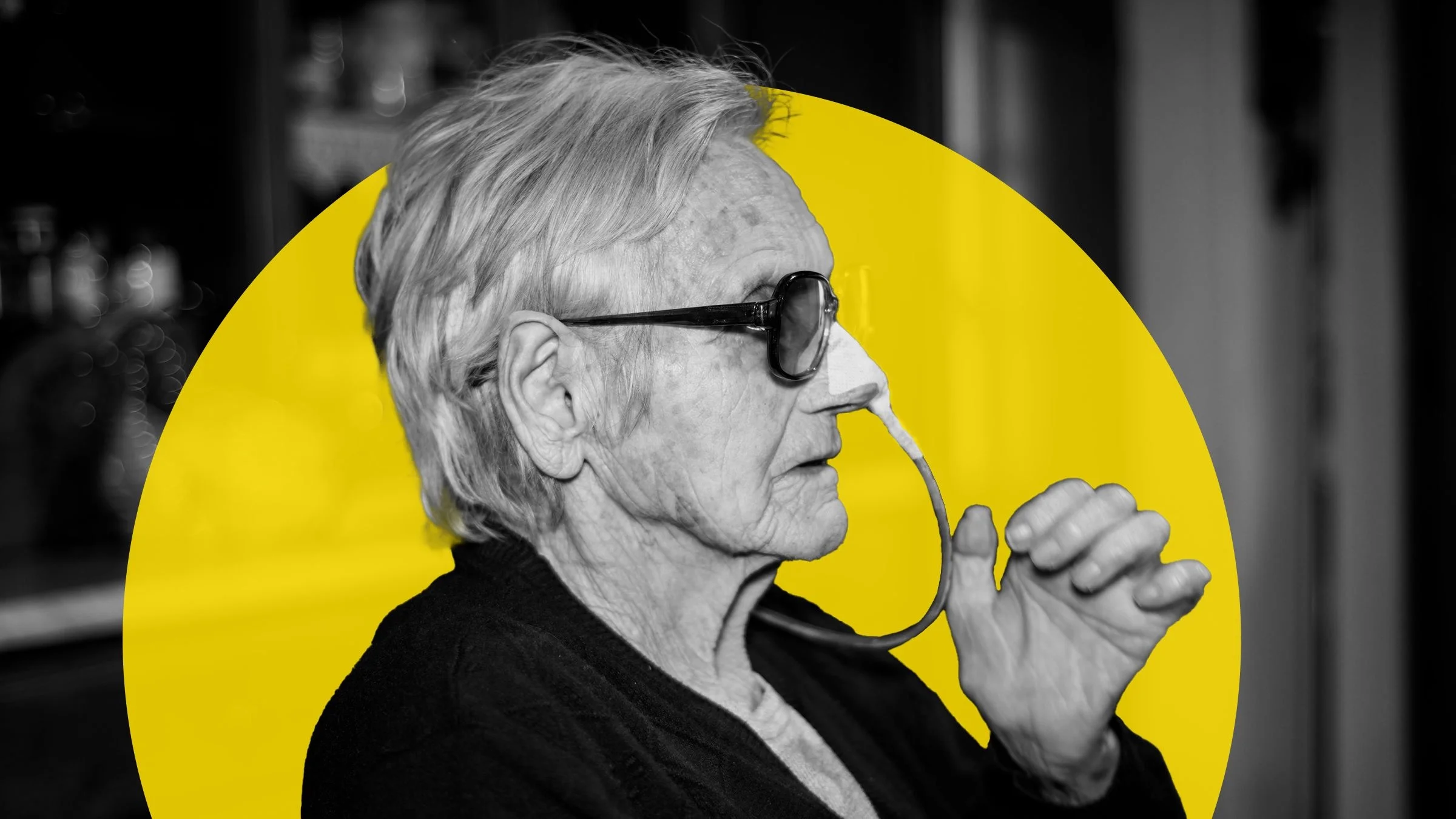 Black-and-white portrait of an older woman with nasogastric tubes in her nose. There is an added graphic yellow circle behind her.