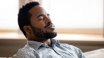 Health: Mental health: man taking deep breathe on couch-1203044203