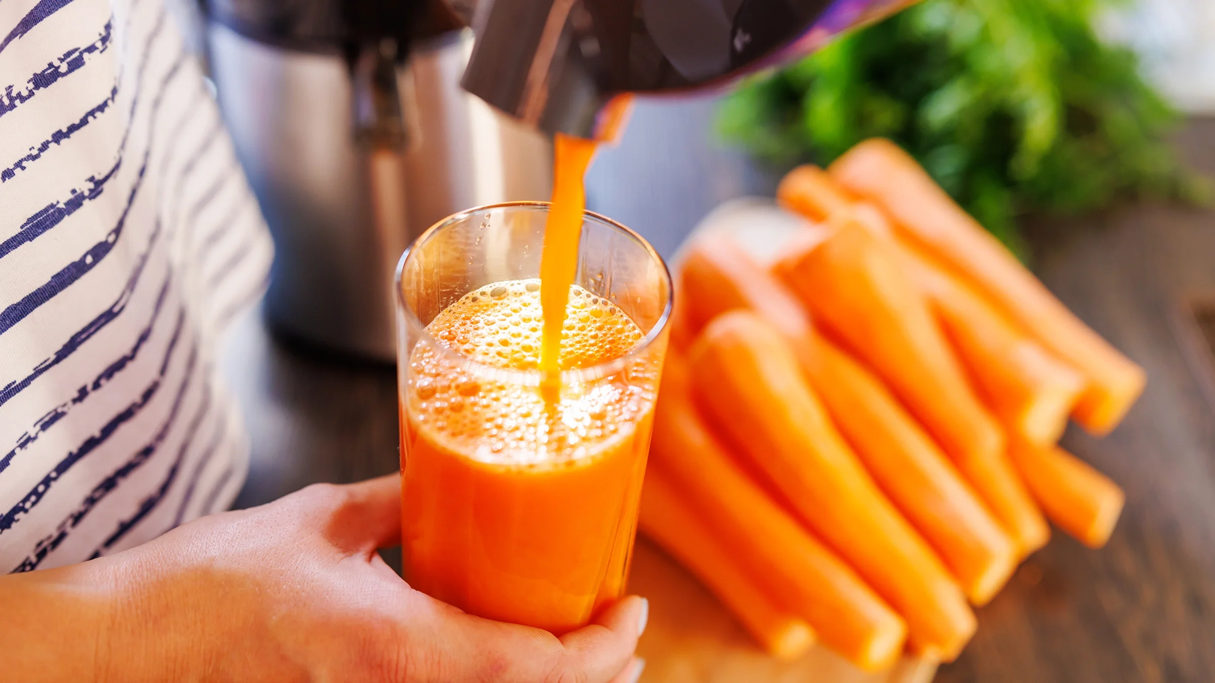 Close-up pouring fresh carrot juice into glass.