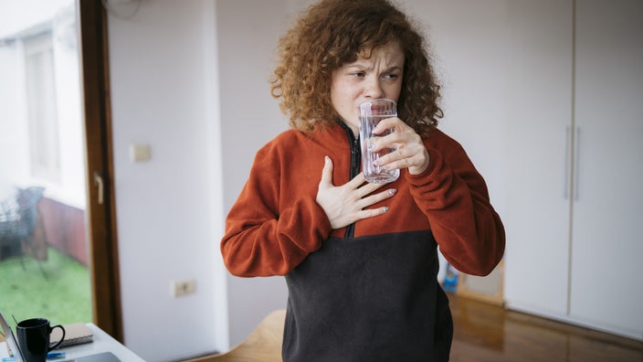 A woman feels digestive discomfort and drinks a glass of water.
