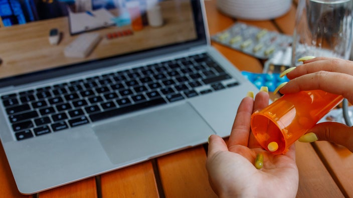 A cropped shot of a person pouring out pills from a bottle in a telehealth appointment. 