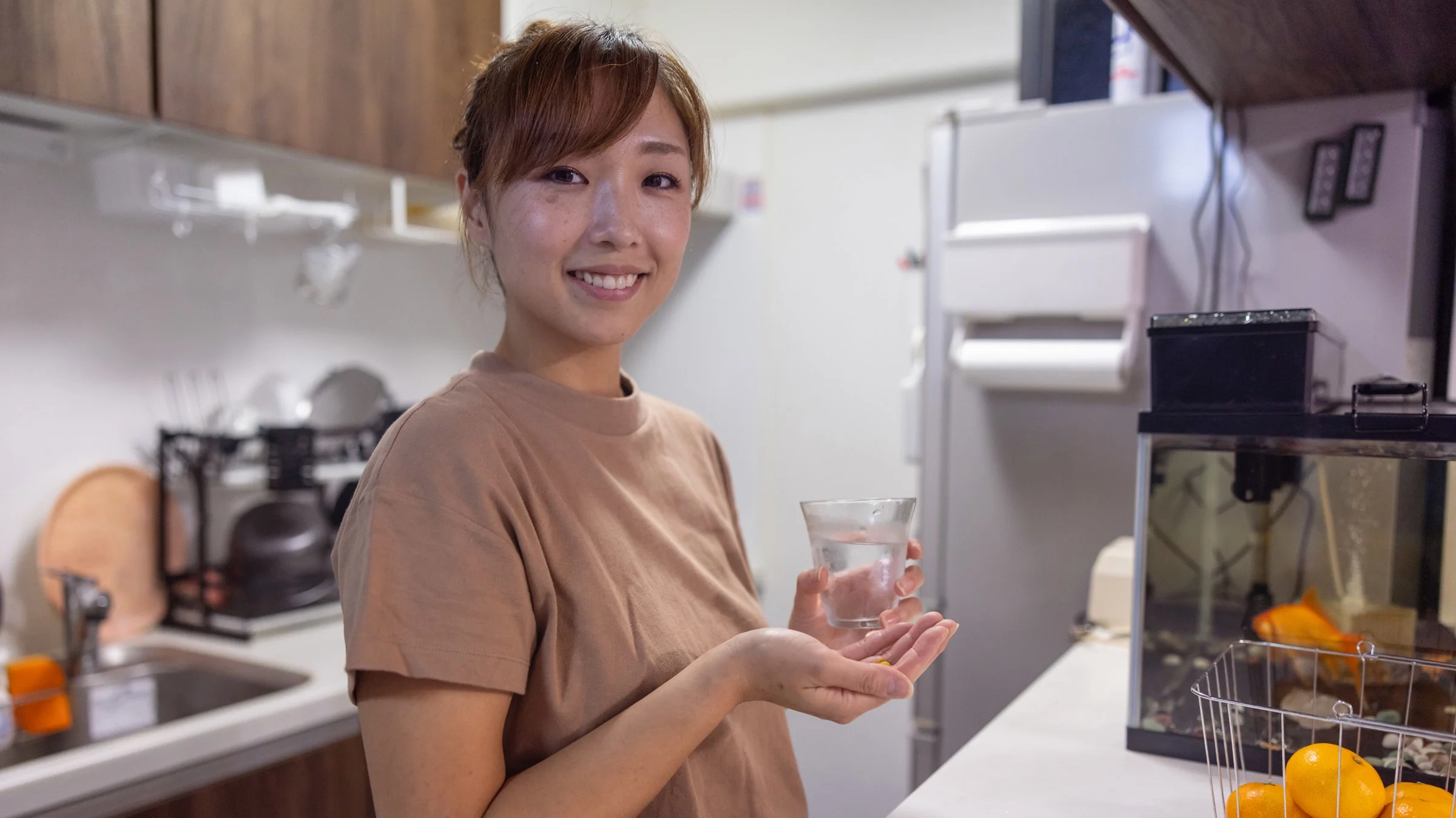 A person standing in a kitchen and taking a pill.