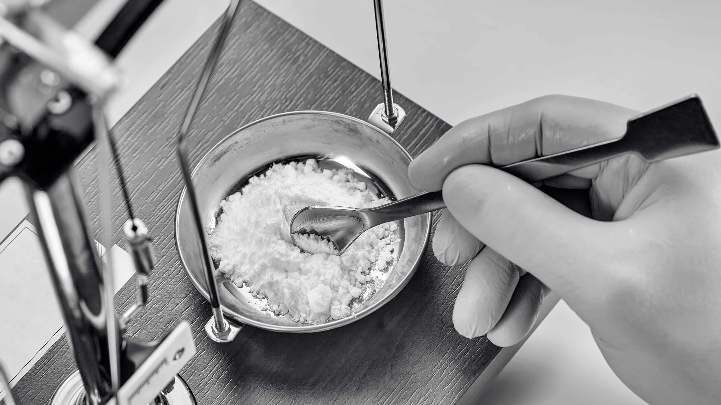 Black and white close-up of a pharmacist weighing and mixing white powder in the lab.