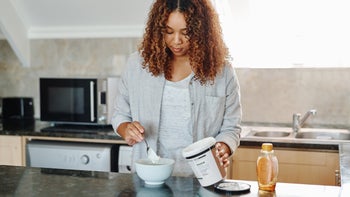 Health: supplements herbs: woman in kitchen serving herself yogurt-1019384888
