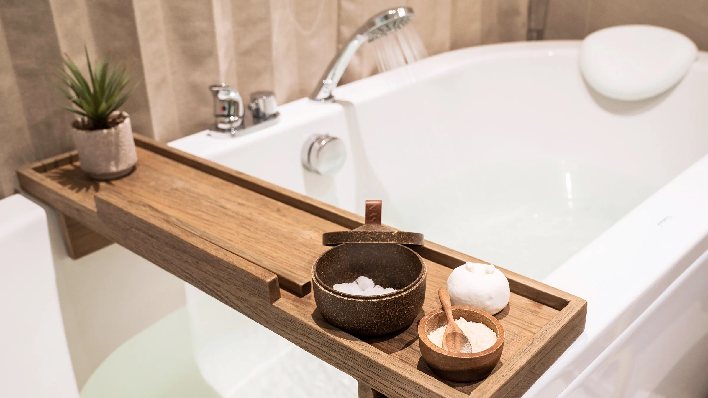 There is a bathtub with wooden table and bath salts