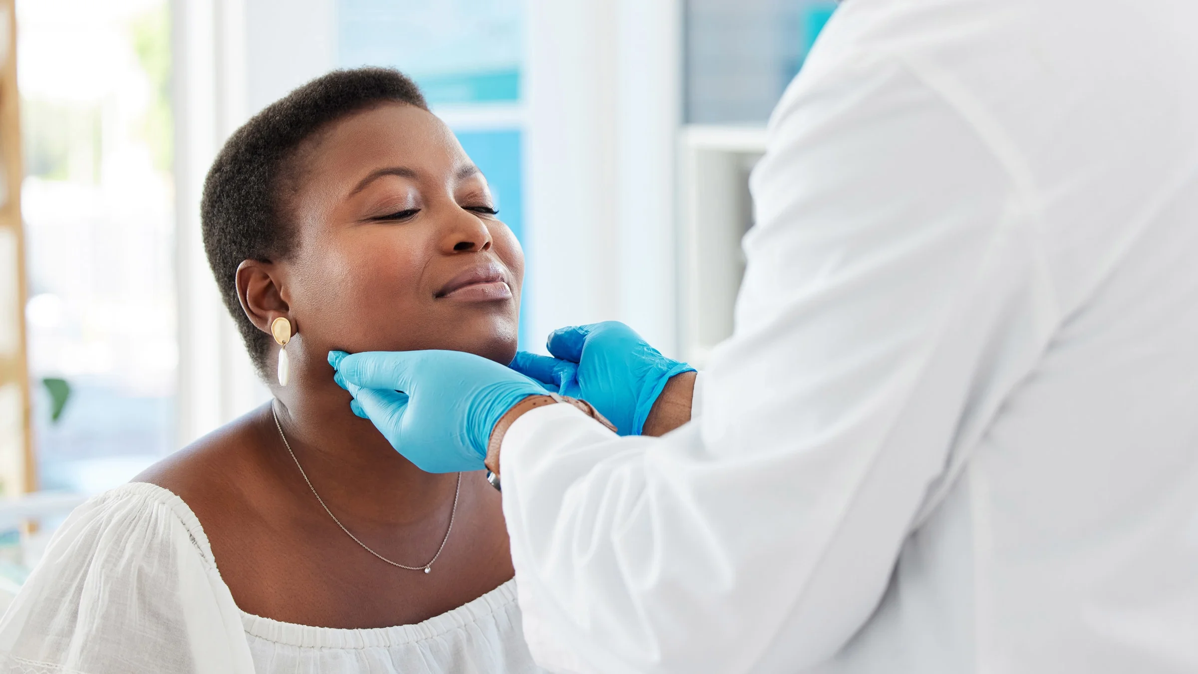 A doctor's hands checking a patient's thyroid.