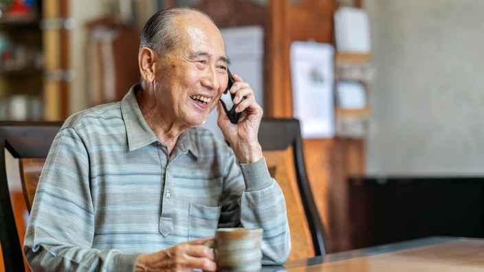 A senior man smiles while having a conversation on the phone.