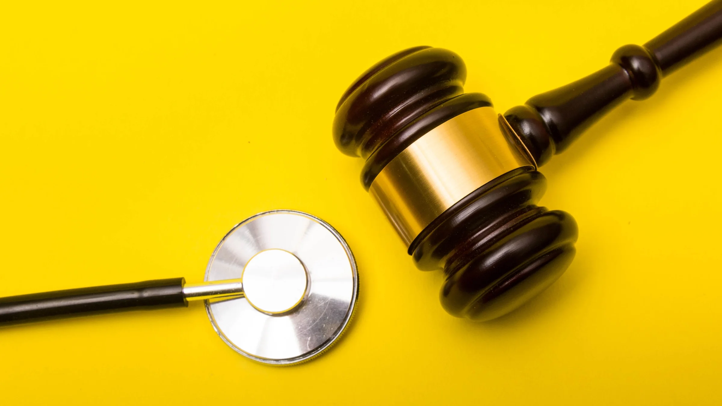 Court gavel and stethoscope on a yellow background.