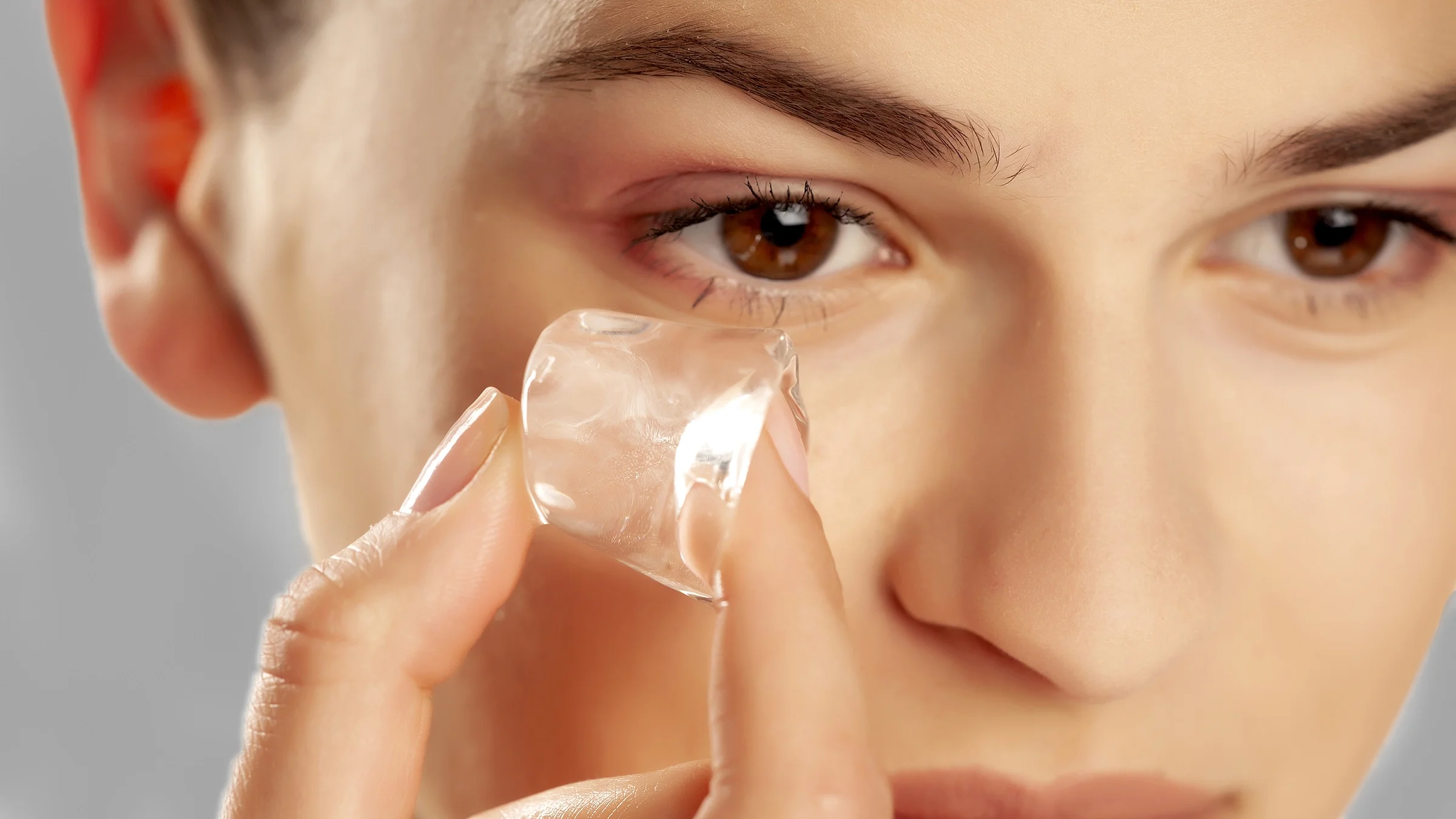 A woman holds an ice cube under her eye.