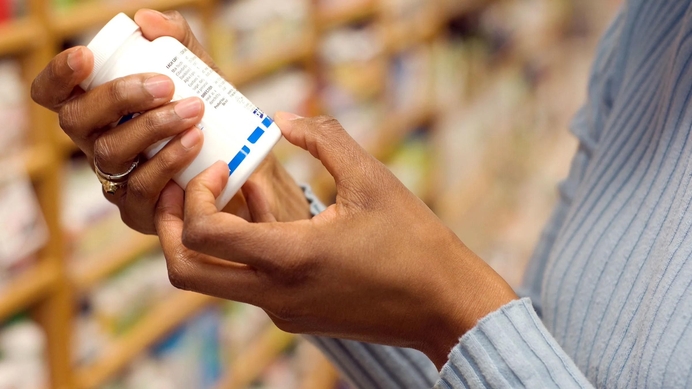 A close-up of a shopper reading a label on a medication bottle.