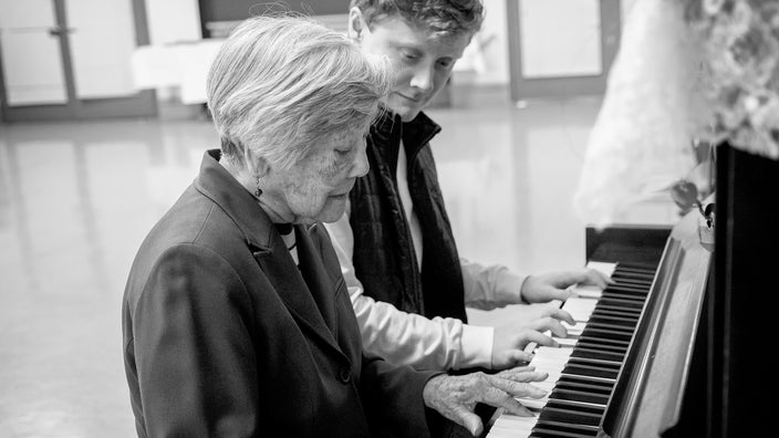 Black and white image of a senior woman playing piano next to a young boy.