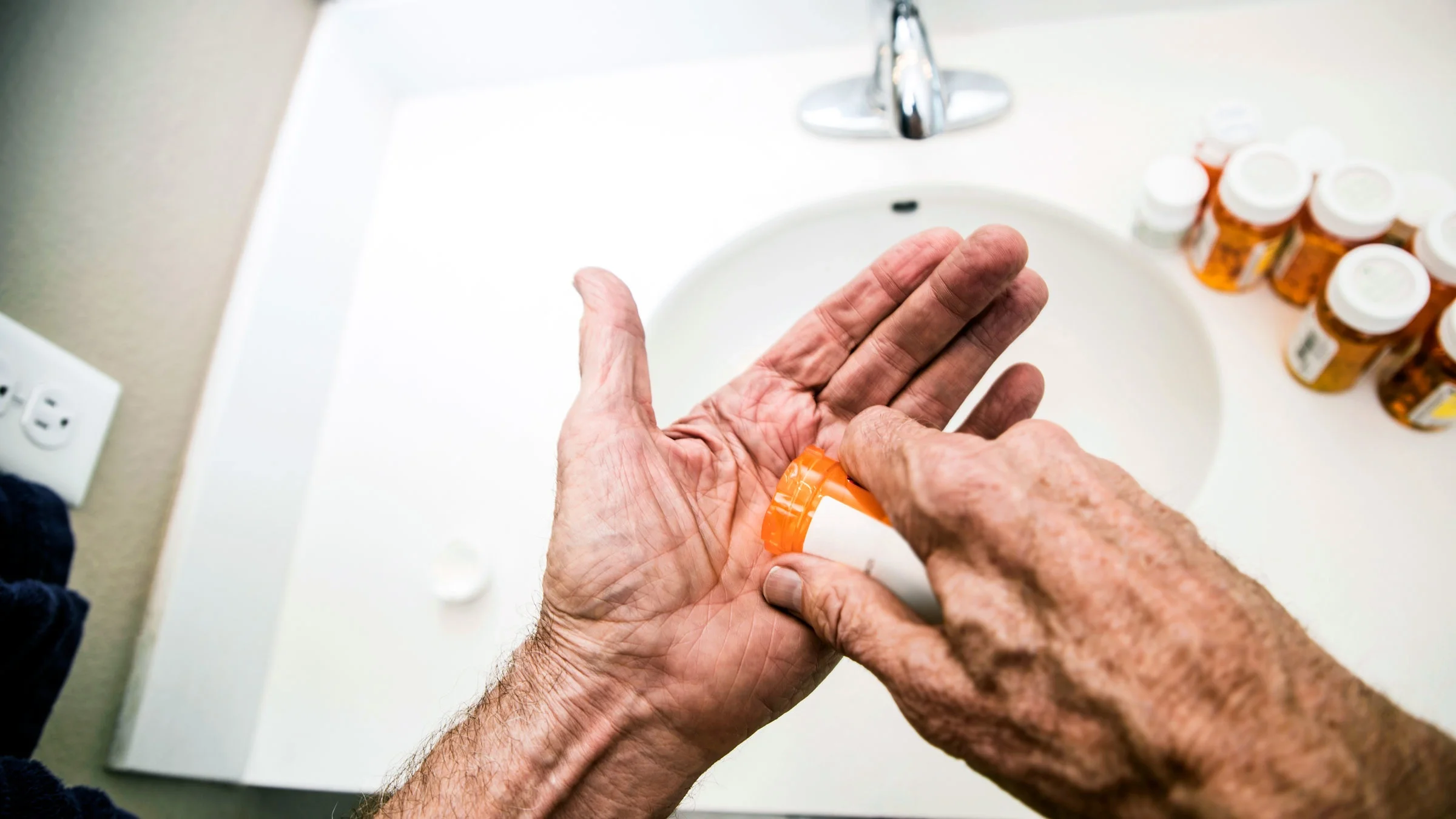 Close-up hand holding pills over sink.