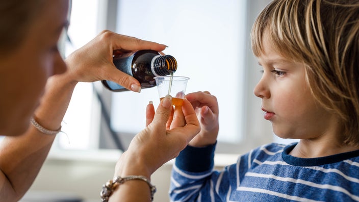 A mother measures out a dose of cough medicine for her child.