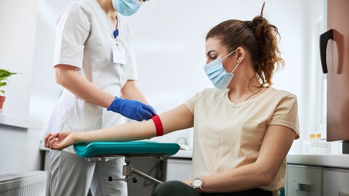 A phlebotomist is preparing a woman for a blood draw.