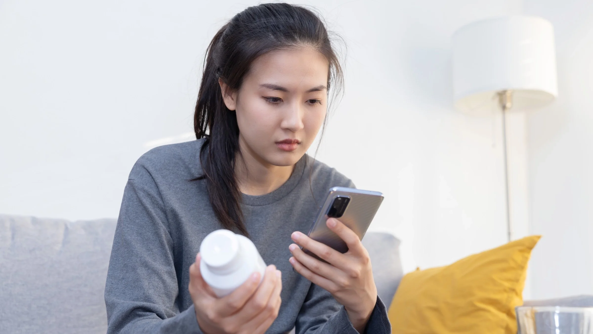 A person holding a pill bottle and looking it up on their phone.