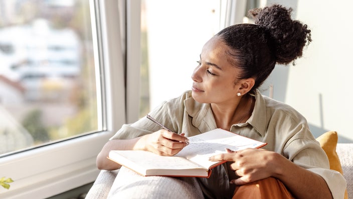 A woman sits on a sofa and writes in a journal.