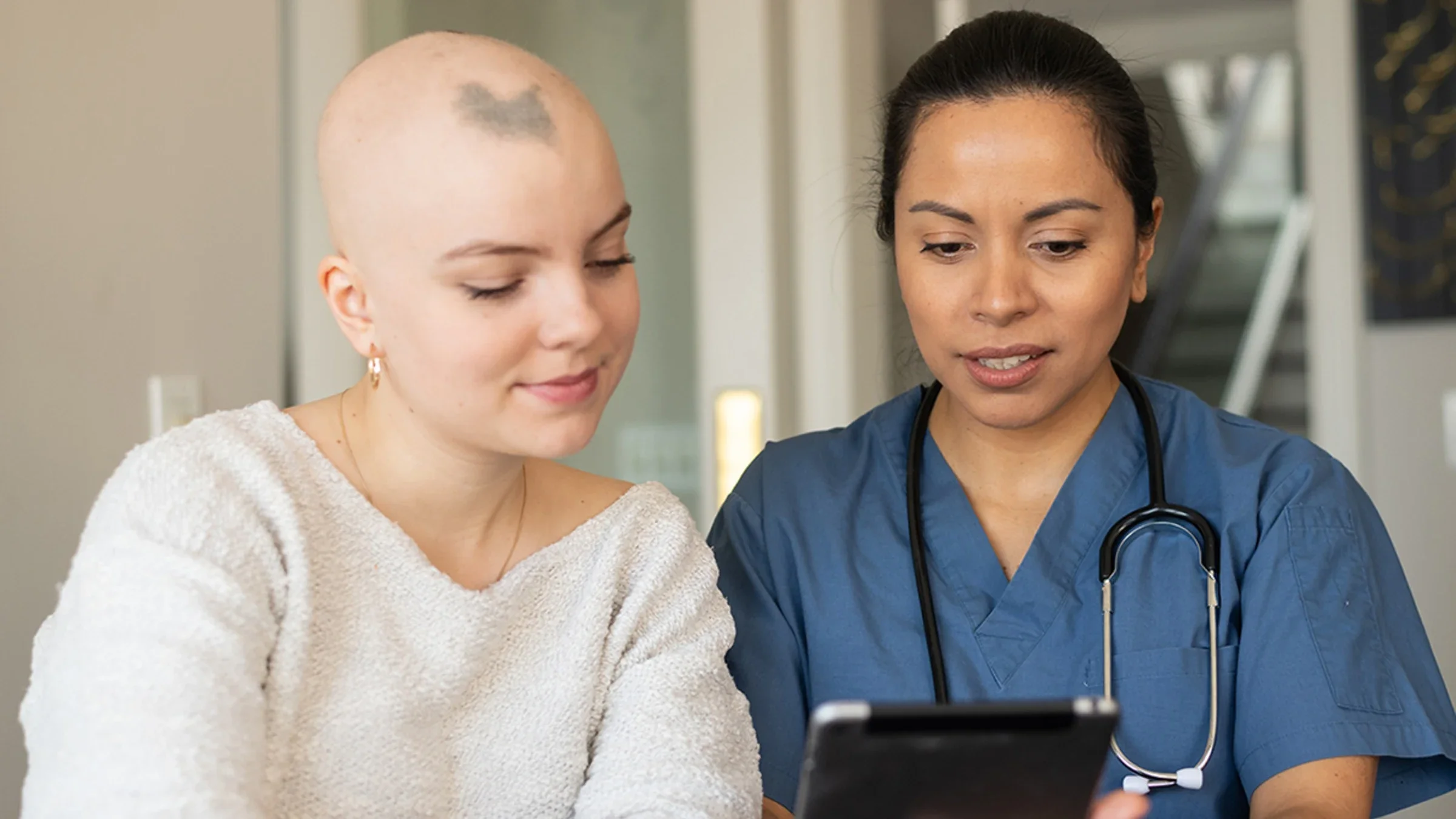 Woman with alopecia talking with her nurse reviewing information on a tablet.
FatCamera/E+ via Getty Images