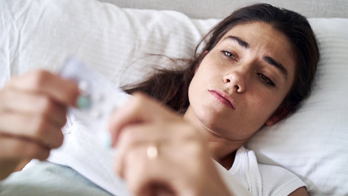 A woman holds a blister pack of pills while lying in bed.