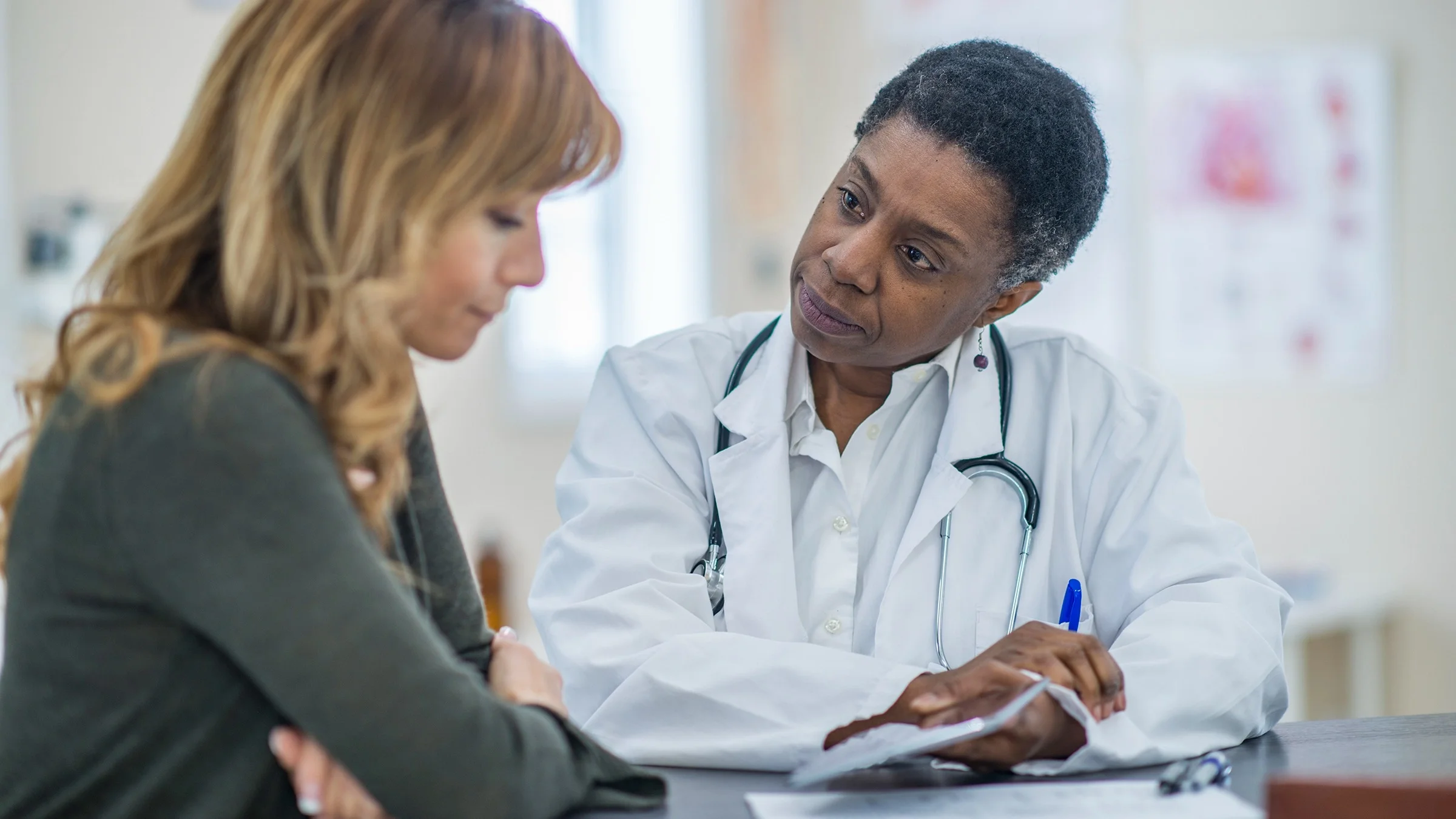 Doctor reviewing paperwork with a patient at a desk in the exam room.