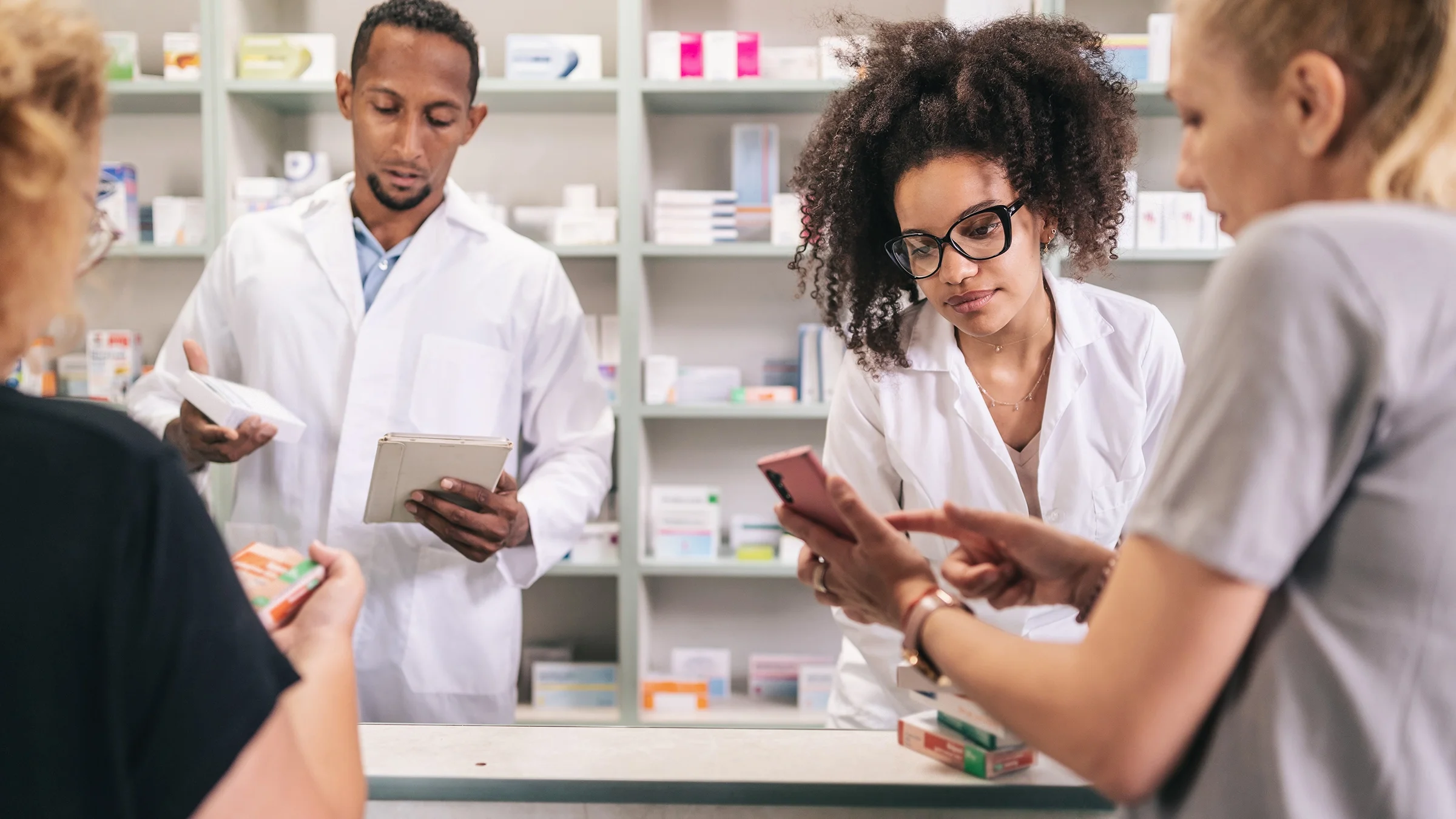 Pharmacists dispense prescription medications to customers in a pharmacy.