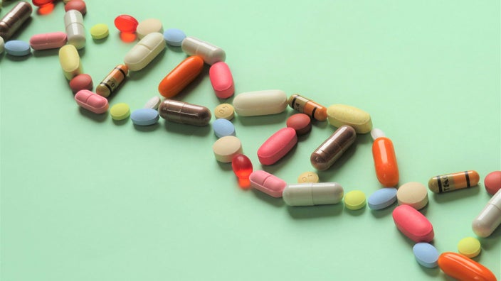 Various colorful pills laid out in the shape of a DNA helix on a light green background.