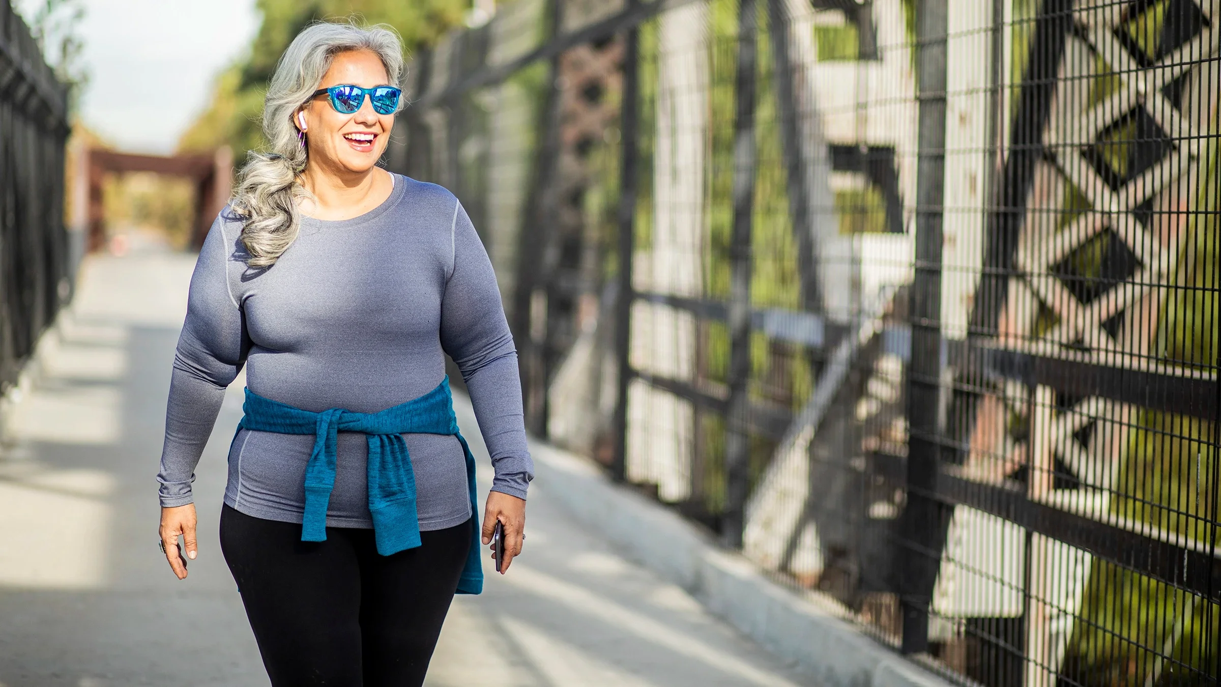 Woman with long silver hair walks on a bridge with sunglasses on.