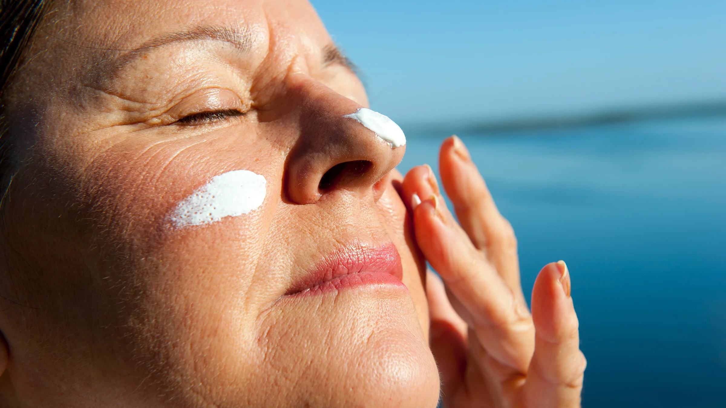 Close-up woman applying sunscreen to her face.