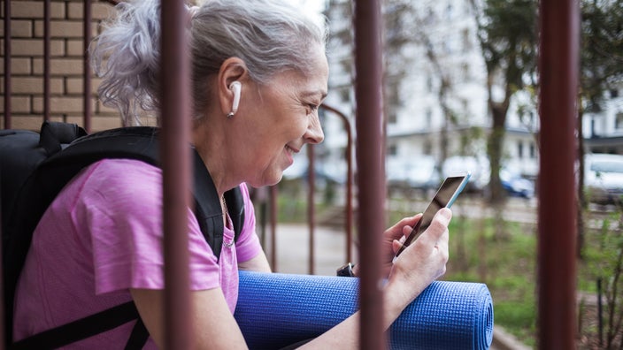 Older woman wearing ear buds and using a smartphone.