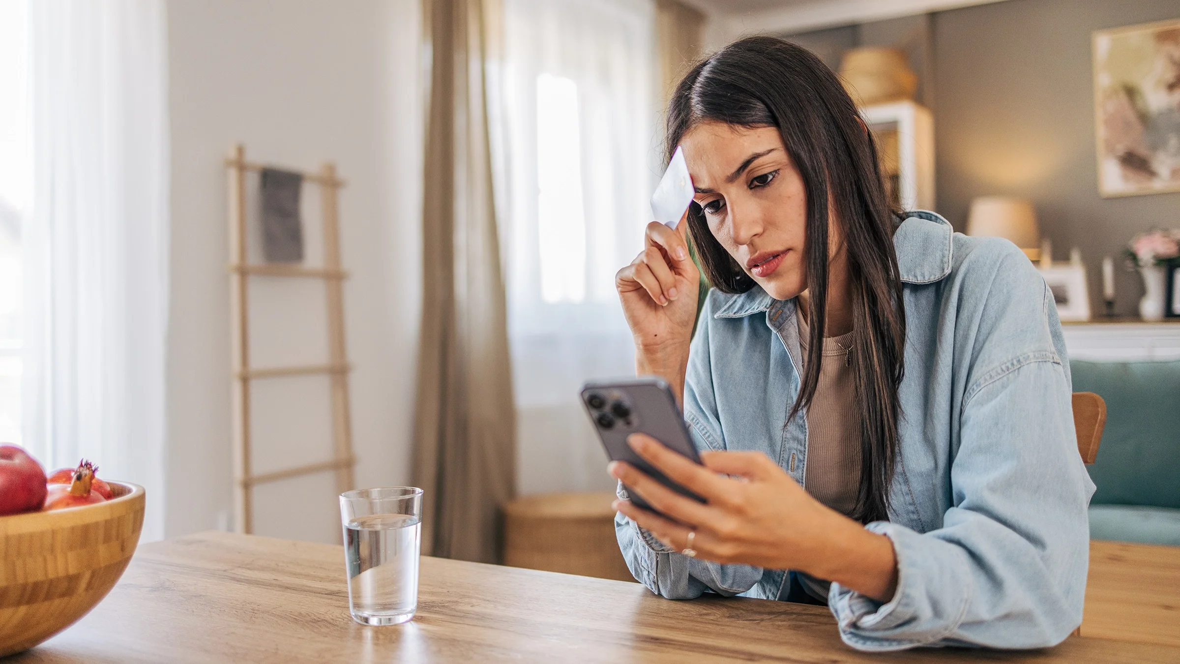 Worried woman using her smartphone and holding credit card
