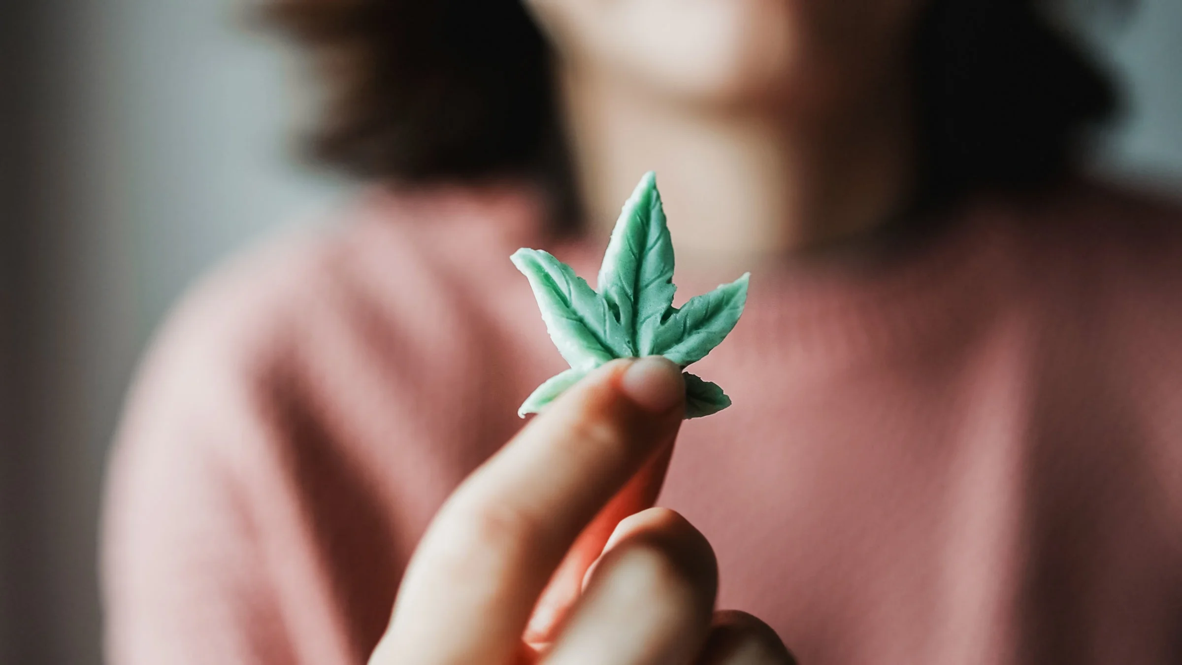 A close-up of a woman holding a cannabis leaf edible gummy.